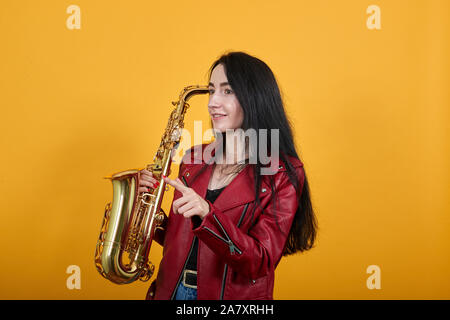 Schöne junge Frau suchen, zeigen Zeigefinger beiseite, Saxophon halten Stockfoto