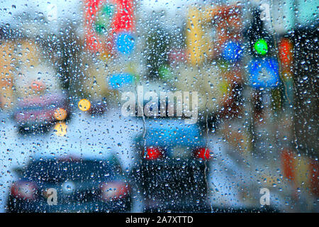 Regen vor dem Fenster auf dem Hintergrund der Lichter der Stadt. Tropfen Wasser fällt auf Glas bei Regen. Wassertropfen über Fenster Glas während es regnete. Stockfoto