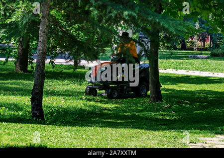 Ein erfahrener Arbeiter mäht Gras mit einem rasentraktor im Garten, Sofia, Bulgarien Stockfoto