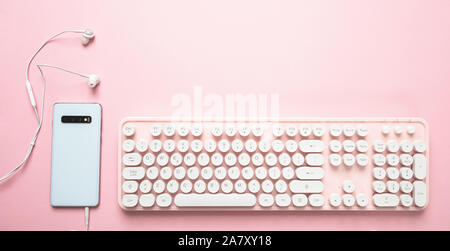 Weibliche Büro Schreibtisch. Handy Rückseite Farbe Weiß mit Kopfhörer und PC-Tastatur gegen rosa Farbe Hintergrund, Stockfoto
