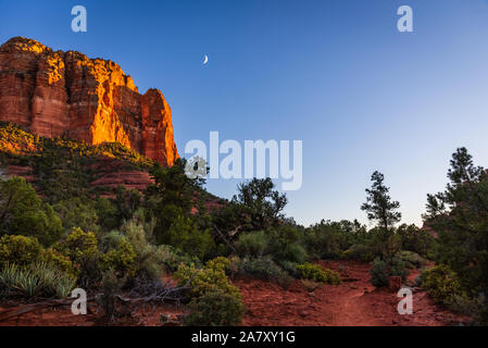 Abendlicher Blick von Sedona Bell Rock von der Bell Rock Trail mit einem waxing Crescent Moon in den Himmel. Stockfoto