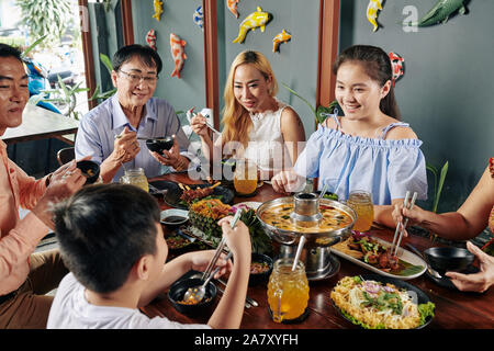 Große glückliche vietnamesische Familie essen leckere Gerichte der asiatischen Küche am grossen Tisch im Restaurant Stockfoto