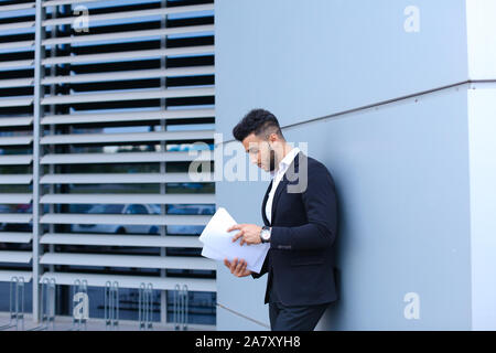 Junge Unternehmer Asiaten hält und hält, liest und sortiert Papiere, steht in der Nähe der Wand des Business Center. Stockfoto