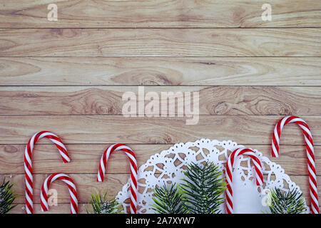 Saisonale Weihnachten flach mit weißer Spitze Deckchen, Zuckerstangen und Tannenzweigen mit Schnee auf Holz- Kopie Raum Hintergrund Stockfoto