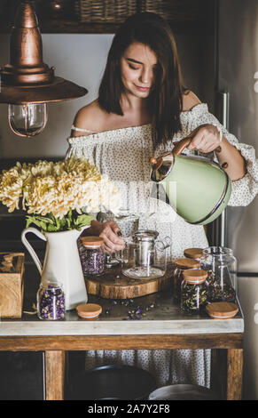 Junge Frau Teezubereitung in Glas Topf an kithcen Zähler Stockfoto