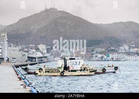 DEC 1, 2018 Hakkodate, Japan -  Hakkodate port Toyokawa pier with fishing boats in winter foggy atmosphere and mount Hakkodate in background. Stockfoto