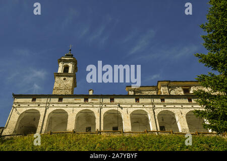 Low Angle View des Heiligtums von St Magno mit einer alten Arcade und dem Glockenturm aus Stein gegen den klaren blauen Himmel, Castelmagno produzieren, Piemont, Italien Stockfoto