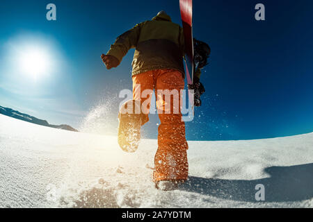 Snowboarder geht bergauf mit Snowboard in den Händen. Backcountry Skiing Konzept Stockfoto