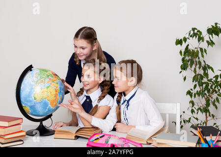 Drei Mädchen mit Büchern und einem Globus in Geographie Klasse am Schreibtisch Stockfoto