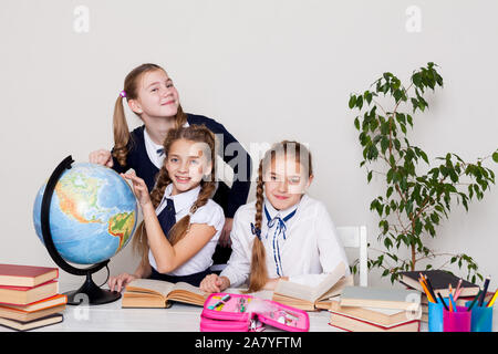 Drei Mädchen mit Büchern und einem Globus in Geographie Klasse am Schreibtisch Stockfoto