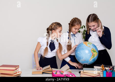 Drei Mädchen mit Büchern und einem Globus in Geographie Klasse am Schreibtisch Stockfoto