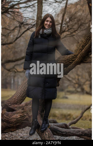 Eine junge Frau geht in den Wald an einem bewölkten Tag. Porträt eines Mädchens in einen warmen Mantel in die Zweige eines Baumes. Stockfoto