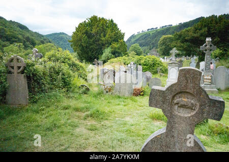 Grabsteine in einem üppig bewachsenen Friedhof von Glendalough, Co Wicklow, Irland Stockfoto