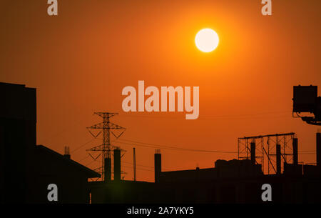 Silhouette Baustelle mit orange Sonnenuntergang Himmel Hintergrund. Hohe Spannung der elektrischen Tower. Schöne große Sonne bei Sonnenuntergang in der Stadt. Dramatischer Himmel Stockfoto