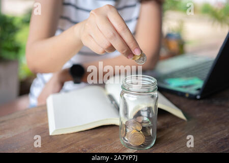 Unternehmerinnen, die Münze in einem Glas, um Geld zu sparen, Geld für Investitionen sparen, Geld ausgeben, wenn sie benötigt wird, und in der Zukunft. Anlagekonzept. Stockfoto