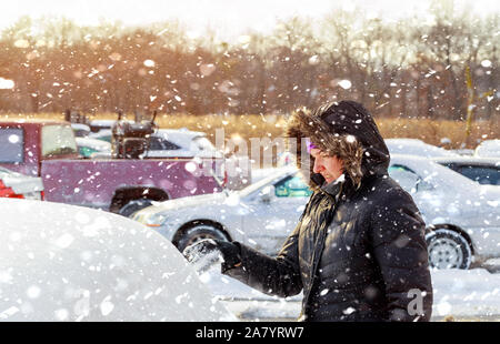 Junge Frau den Schnee von Bürsten in Schneefall sein Auto in einem kalten Winter Tag Stockfoto