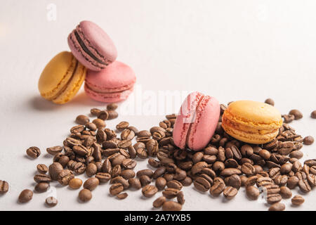 Kaffeebohnen close-up auf einem hellen Hintergrund verstreut. Macarons liegen auf der Oberseite Stockfoto