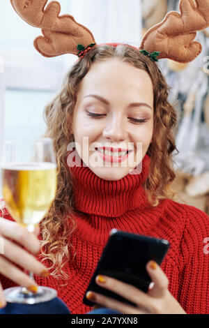 Porträt der jungen fröhliche Frau mit Glas Sekt beim Senden von SMS-Nachrichten an Freunde Stockfoto