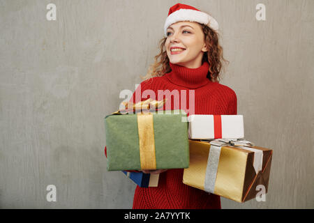Glückliche junge Kaukasier Frau in Santa hat viele Weihnachtsgeschenke Stockfoto