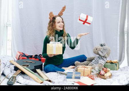 Gerne Begeistert junge Frau werfen giftboxes in der Luft beim Sitzen auf dem Boden in Ihrem Zimmer Stockfoto