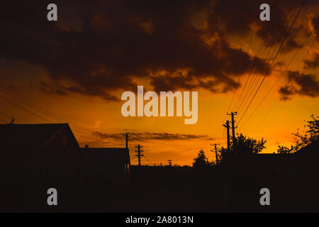 Silhouette von Stromleitungen und Häuser unter orange Sonnenuntergang Himmel mit Wolken. Stockfoto