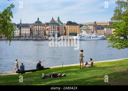 Skeppsholmen Stockholm, Aussicht im Sommer von Menschen entspannen in der Amiralitetsparken auf der Insel Skeppsholmen mit Gamla Stan in der Ferne, Stockholm Stockfoto