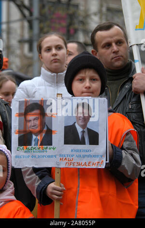 Die Orange Revolution in der Ukraine. Junge gekleidet Orange die Demonstration von ukrainischen Migrantinnen in der Tschechischen Republik Ukrainischen oppositionellen Präsidentschaftskandidaten Viktor Juschtschenko am Wenzelsplatz in Prag zu unterstützen besucht, der Tschechischen Republik, am 28. November 2004. Die Inschrift unter dem Porträt des Präsidentschaftskandidaten Viktor Janukowitsch (L) ist Bandukovych (buchstäblich ein Bandit oder ein Räuber) geändert. Die Inschrift unter dem Porträt des Präsidentschaftskandidaten Viktor Juschtschenko (R) wird mit den Worten "unser Präsident" hinzugefügt. Stockfoto