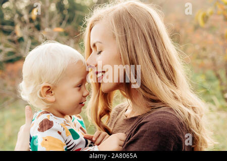 Die Mutter küsst zärtlich, während Ihr Kind in ihren Armen außerhalb Holding. Stockfoto
