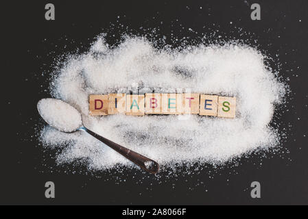 Haufen Zucker mit Wort DIABETES auf schwarzem Hintergrund. Konzept der Diabetes, Gesundheit und ungesundes Essen Stockfoto
