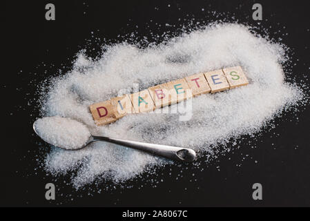 Haufen Zucker mit Wort DIABETES auf schwarzem Hintergrund. Konzept der Diabetes, Gesundheit und ungesundes Essen Stockfoto