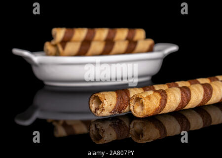 Gruppe von fünf ganze crunchy beige Haselnuss gerollte Waffel Keks in weiße, ovale Keramik Schüssel auf schwarzem Glas isoliert Stockfoto
