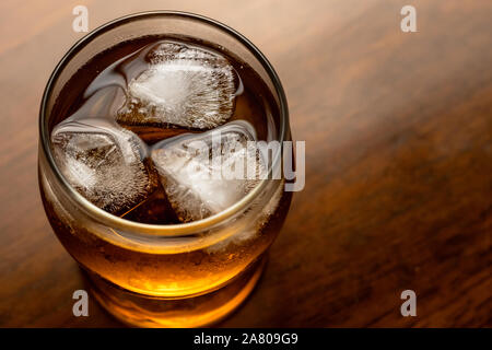 Glas Whisky mit Eis auf Holz- Hintergrund. Bourbon auf dunklem Holz Tisch. Alkohol braun Drink mit Blasen. Rum, Top View close-up gekühlt. Text spac Stockfoto