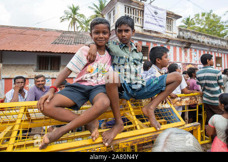 Zwei Jungen auf einem gelben Zaun beobachten die Kutti Kudithal Festival in Trichy, Tamil Nadu, Indien sitzen Stockfoto