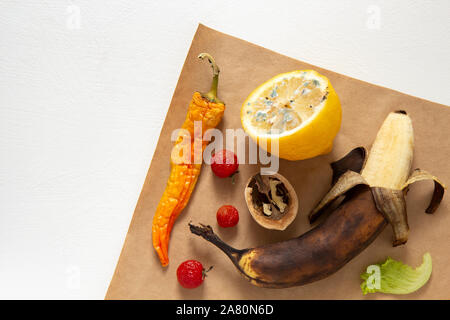 Hässliches Essen. Verdorbene Produkte liegen auf braunem Papier auf einem weißen Hintergrund. Horizontale Ausrichtung, Ansicht von oben. Stockfoto