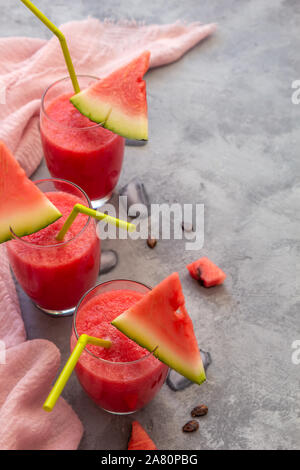 Drei Wassermelone Saft in Gläser mit rosa Tuch auf grauem Beton Tabelle. Vertikale Ausrichtung, Kopie Raum Stockfoto