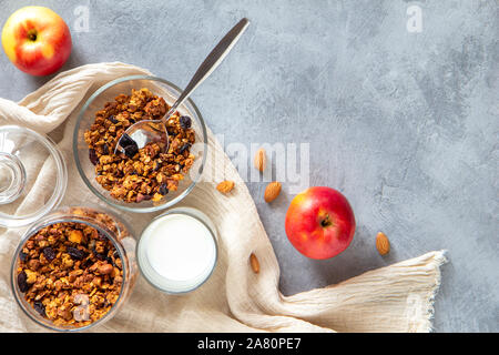 Müsli mit Zimt, Honig und Äpfel in eine Glasschüssel, Milch, Äpfel auf einem grauen Beton Tabelle. Flach, Kopieren Raum Stockfoto