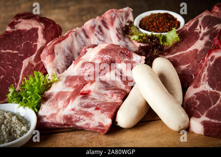 Teile der raw Spare Ribs, Beef Steak und Wurst aus Schweinefleisch oder Kalbfleisch bereit für ein BBQ mit Gewürzen in Schalen angezeigt in der Nähe zu sehen, geeignet für Metzger Stockfoto