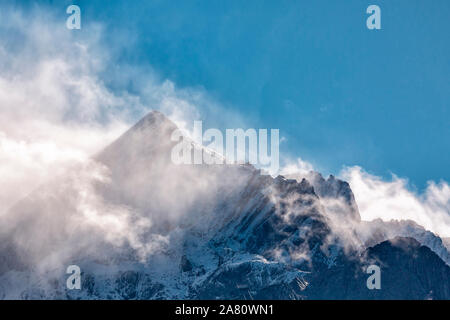 Die schneebedeckten Gipfel der Alpen gegen den blauen Himmel. Eine leichte weiße Wolke liegt auf dem Gipfel des Berges. Stockfoto