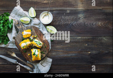 Frisch gebackene Maiskolben mit Aioli Sauce und Koriander auf rustikalen Holzmöbeln Hintergrund. Gesunde vegetarische Nahrung. Ansicht von oben. Platz für Text. Stockfoto