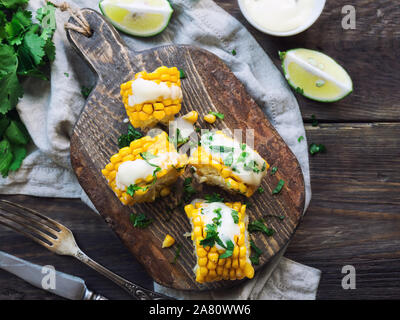 Frisch gebackene Maiskolben mit Aioli Sauce und Koriander auf rustikalen Holzmöbeln Hintergrund. Gesunde vegetarische Nahrung. Ansicht von oben. Stockfoto