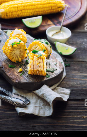 Frisch gebackene Maiskolben mit Aioli Sauce und Koriander auf rustikalen Holzmöbeln Hintergrund. Gesunde vegetarische Nahrung. Stockfoto