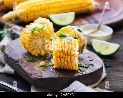 Frisch gebackene Maiskolben mit Aioli Sauce und Koriander auf rustikalen Holzmöbeln Hintergrund. Gesunde vegetarische Nahrung. Stockfoto