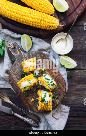 Frisch gebackene Maiskolben mit Aioli Sauce und Koriander auf rustikalen Holzmöbeln Hintergrund. Gesunde vegetarische Nahrung. Ansicht von oben. Stockfoto