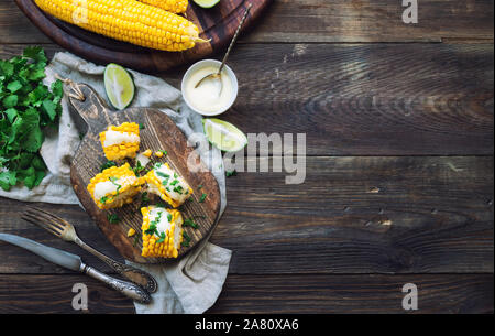 Frisch gebackene Maiskolben mit Aioli Sauce und Koriander auf rustikalen Holzmöbeln Hintergrund. Gesunde vegetarische Nahrung. Ansicht von oben. Platz für Text. Stockfoto