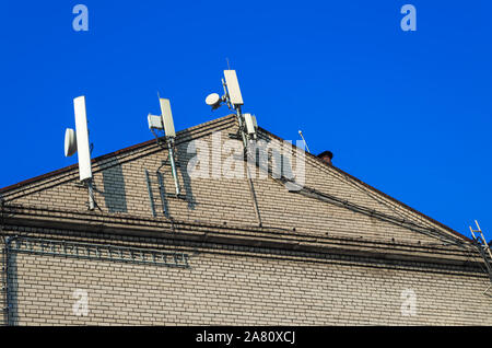 Antennen, Halterung und Kabel der zellularen Kommunikation sind auf das Gebäude Giebel gegen den blauen Himmel entfernt Stockfoto