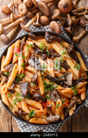 Penne Pasta mit Pilzen Honig Pilze, Tomaten, Käse und Petersilie close-up in einem Teller auf dem Tisch. Vertikal oben Ansicht von oben Stockfoto