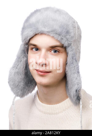 Kopf und Schultern studio Portrait von lächelnden Teenager boy trägt blaue aus Fellimitat winter Trapper Hut (Ushanka) und Pullover auf weißem Hintergrund Stockfoto