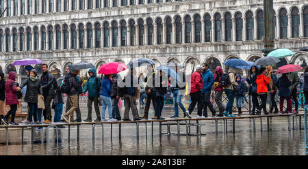 Touristen in einer regnerischen Venedig mit duckboards über eine überschwemmte St Mark's Platz bei Flut zu gehen Stockfoto