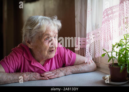 Ältere Frau sieht traurig aus dem Fenster. Stockfoto