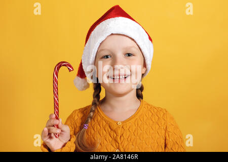 Happy kleines Mädchen in santa hut mit Weihnachten Süßigkeiten. Ein Kind auf einem gelben Hintergrund. Stockfoto